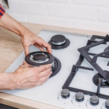 Man hand install burner ongas hob in kithen, close up. Repairs of gas control panel