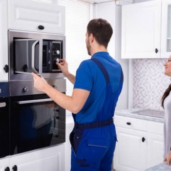 Happy Young Woman Standing Near Technician Adjusting Temperature Of Oven